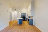 Located at 501 NW Seventh Terrace in Fort Lauderdale, FL, this modern one-bedroom, one-bathroom residence offers a thoughtfully designed open-concept layout with impressive soaring ceilings throughout. Light wood-tone flooring flows seamlessly across the living, dining, and kitchen areas, creating a bright and cohesive aesthetic.

The kitchen is a standout feature, showcasing two-tone cabinetry with crisp white upper cabinets and bold blue lower cabinets, complemented by a white quartz countertop, subway tile backsplash, and stainless steel appliances including a refrigerator, range, and microwave. A central island provides additional prep and seating space, while modern cylindrical pendant lights add a contemporary finishing touch. Large floor-to-ceiling windows and a glass door lead to a private balcony, framing lush tropical palm views and filling the space with abundant natural light.

The spacious bedroom continues the clean, airy design with direct balcony access and generous closet space, including a walk-in closet with built-in wire shelving. The bathroom features large-format tile flooring, a walk-in glass shower with floor-to-ceiling tile surround, a floating vanity with white quartz countertop, and matte black fixtures throughout. Additional conveniences include a dedicated laundry area and ample hallway closets.