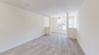 Located at 4301 Cox Pl in Greensboro, NC, this single-floor unit offers a well-organized layout with a neutral color palette and a mix of carpet and hard-surface flooring throughout. The open-concept living and dining area is spacious and bright, featuring plush carpet, a ceiling-mounted light fixture, and a window that allows natural light to fill the space. A ceiling fan with integrated lighting serves one of the carpeted rooms, which also benefits from an outdoor-facing window.

The kitchen is thoughtfully designed with warm honey-toned cabinetry, granite-style countertops, and a peninsula that doubles as a breakfast bar with seating. Black appliances, including a refrigerator, range, and built-in microwave, provide a cohesive look. Light wood-style flooring runs throughout the kitchen, complementing the cabinetry. A pendant lantern fixture above the peninsula adds a decorative touch.

The bathroom features a clean, all-white soaking tub and shower combination with tile surround and light tile flooring. A dedicated laundry room includes washer and dryer hookups, wire shelving for storage, and wood-style flooring. Additional carpeted rooms offer versatile space with crisp white walls and ample room to configure as needed.