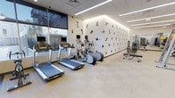This single-floor fitness center offers a clean, contemporary workout environment designed to support a range of exercise routines. The space is outfitted with multiple treadmills and elliptical machines positioned along a large window, allowing natural light to fill the area while providing views to the exterior. The flooring consists of light-toned, tile-style material that contributes to the room's bright and airy feel.

A standout design feature is the bold accent wall adorned with dynamic silhouette illustrations of individuals engaged in various athletic activities, including cycling, skateboarding, and gymnastics. This artistic element adds energy and visual interest to the space, reinforcing its fitness-focused purpose.

Overhead, recessed linear LED lighting runs across the ceiling, ensuring consistent, even illumination throughout the room. The ceiling features a drop-tile grid system, lending a clean and organized appearance. Strength training equipment and benches are visible toward the far end of the room, indicating a well-rounded facility accommodating both cardio and resistance training. The overall ambiance is modern, motivating, and well-maintained.