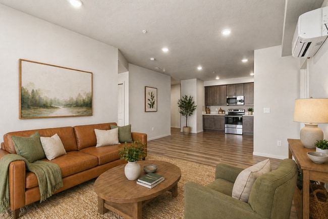 Espacio habitable moderno de concepto abierto con un acogedor sofá de cuero marrón, plantas y una elegante cocina con gabinetes de madera. - Lofts at Garden District