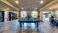Located at 5403 W 96th Ave in Westminster, Colorado, this generously sized single-floor community clubhouse delivers an impressive blend of modern design and warm, lodge-inspired aesthetics. The open-plan layout is anchored by soaring double-height ceilings in the main lounge area, where floor-to-ceiling windows flood the space with abundant natural light and frame views of the surrounding landscape. Pendant globe lighting adds a contemporary touch overhead, complementing the rich wood-look tile flooring that runs throughout.

Stacked stone columns and accent walls lend rustic character, while a stone-surround fireplace with a wood mantel and wall-mounted TV creates a cozy focal point in the game room. A full-size billiards table serves as the centerpiece of this entertainment zone, flanked by built-in bookshelves with a rolling library ladder and warm sconce lighting. A seating nook nearby provides a relaxed retreat.

The fully equipped kitchen features white shaker cabinetry, granite-topped islands, a mosaic tile backsplash, and stainless steel appliances, making it ideal for hosting events. A mezzanine level overlooks the main floor, adding architectural depth. Together, these elements create a sophisticated yet inviting communal gathering space.