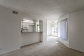 Located at 1256 W Arrow Hwy in Upland, California, this single-floor residential unit offers a clean, functional layout designed for comfortable everyday living. The open living area is finished with wall-to-wall carpet in a neutral tone and features a textured ceiling, crisp white walls, and a sliding glass door fitted with vertical blinds that allows natural light to fill the space. A half-wall peninsula connects the living area to the galley-style kitchen, which is equipped with white cabinetry, granite-style laminate countertops, a coil-burner electric range, built-in microwave, dishwasher, and a sink — all set above wood-look vinyl plank flooring. The bedrooms are carpeted and well-proportioned, with one featuring a sliding closet and direct access to a bathroom with a vanity, granite-style countertop, white cabinetry, and a tub/shower combination. A second bathroom mirrors this layout with a tub/shower and wood-look flooring. Throughout the unit, the neutral color palette and consistent finishes create a clean and cohesive aesthetic, while multiple windows provide natural light across the floor plan.