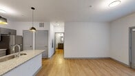 This contemporary 610-square-foot apartment offers a thoughtful layout maximizing space and functionality. The heart of the home is the open-concept kitchen, boasting sleek gray cabinetry, granite countertops, and stainless steel appliances. Two stylish pendant lights illuminate the kitchen island, which serves as both a prep area and casual dining space.

The living area flows seamlessly from the kitchen, featuring warm wood-look flooring that extends throughout the apartment. The spacious 140-square-foot bedroom is carpeted for comfort and includes two windows, providing natural light and ventilation. The bathroom is modern and efficient, with a granite-topped vanity, large mirror, and contemporary lighting.

Storage is ample, with a dedicated closet space featuring wire shelving systems. The apartment's neutral color palette, dominated by whites and grays, creates a bright and airy atmosphere. High ceilings and recessed lighting further enhance the sense of spaciousness.

This well-designed single-floor apartment effectively balances style and practicality, offering a comfortable living space in a compact footprint. Its modern amenities and thoughtful layout make it an ideal choice for singles or couples seeking a contemporary urban living experience.