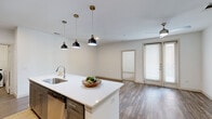 Located at 2814 Race St in Fort Worth, TX, this thoughtfully designed 2-bedroom, 2-bathroom home offers a seamless blend of modern style and functional living. The open-concept kitchen and living area serves as the heart of the home, anchored by a striking oversized island with a crisp white quartz countertop, stainless steel sink, and a trio of black-and-brass pendant lights that add a contemporary flair. The kitchen is further equipped with gray shaker cabinetry, a warm herringbone tile backsplash, stainless steel appliances, and recessed lighting. Wood-look flooring flows throughout the main living areas, complemented by a ceiling fan that enhances comfort and airflow. Natural light enters through large windows and a glass door leading to an outdoor area. The primary bedroom is generously sized, featuring plush carpet, a ceiling fan, and a bright window with exterior views. The second bedroom offers wood-look flooring and convenient access to an adjacent space. Both bathrooms are finished with gray vanity cabinetry, white countertops, and elegant marble-style tile surrounding the bathtub and shower. A dedicated laundry room houses a full-size washer and dryer, adding everyday convenience. Two closets provide ample storage throughout.
