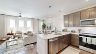This single-floor residence is thoughtfully designed with a cohesive aesthetic that balances modern functionality and warm, inviting style. The open-concept kitchen serves as the heart of the home, showcasing rich dark-stained shaker cabinetry, a textured tile backsplash, stainless steel appliances, and a generous quartz-topped peninsula with bar seating illuminated by glass pendant lights. The kitchen flows naturally into the living and dining areas, where hardwood-style flooring, large windows, and a ceiling fan contribute to a bright, airy atmosphere.

The dining area benefits from natural light through sizable windows dressed with sheer curtains, while the living room offers ample space for relaxation. The bedrooms feature plush carpeting, generous windows, and walk-in closet access, providing comfortable and functional retreats.

The bathrooms are finished with large-format tile flooring, dark wood vanity cabinetry, and white quartz countertops. The primary bath includes a frameless glass-enclosed walk-in shower with subway tile surround, while an additional bathroom features a dual-sink vanity with a tall storage tower. Throughout the residence, clean white walls and consistent finishes create a polished, cohesive living environment.