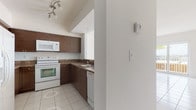 This single-floor residence offers a clean, bright interior with a thoughtfully designed layout. The open living and dining area is finished with large white tile flooring and fills with natural light through sliding glass doors that lead to a private balcony, offering open outdoor views of the surrounding landscape and palm trees. A pendant light fixture anchors the dining space, adding a subtle design touch.

The kitchen is efficiently laid out in a U-shape configuration, featuring rich dark wood cabinetry with brushed hardware, stone-look countertops, white appliances including an electric range, built-in microwave, and dishwasher, all set on matching white tile flooring. Recessed track lighting provides focused illumination throughout.

The bedrooms are carpeted for comfort, with the primary bedroom benefiting from sliding glass door access to the balcony and views beyond. A second bedroom offers a large window that brings in ample natural light. The primary suite includes a generously sized walk-in closet equipped with built-in shelving on both sides.

Both bathrooms are finished in crisp white tile, each featuring a single-sink vanity with under-cabinet storage and a large mirror. The primary bathroom includes a full tub and shower combination, while the secondary bathroom offers a shower. The overall aesthetic throughout is clean, light, and move-in ready.