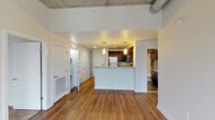This single-floor unit showcases a compelling blend of industrial and contemporary design elements throughout. The open living area is defined by rich hardwood flooring and soaring exposed concrete ceilings with visible ductwork, lending an urban loft aesthetic to the space. Large windows frame sweeping city skyline views, filling the area with natural light.

The kitchen is thoughtfully designed with dark espresso cabinetry, granite countertops, stainless steel appliances including a range, microwave, and refrigerator, and a peninsula that provides additional prep and seating space. Pendant lighting adds a refined touch above the peninsula.

The bedrooms feature plush carpeting and continue the industrial-chic theme with exposed concrete ceilings and ductwork. Each room benefits from generous windows overlooking the urban landscape below.

The bathroom is well-finished, featuring dark espresso cabinetry, granite countertops, large-format tile flooring, and a tub-shower combination with patterned tile surround. A dedicated in-unit laundry area adds everyday convenience. The overall ambiance is modern and urban, with a cohesive palette of neutral tones and quality finishes throughout.