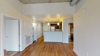 This single-floor unit showcases a compelling blend of industrial and contemporary design elements throughout. The open living area is defined by rich hardwood flooring and soaring exposed concrete ceilings with visible ductwork, lending an urban loft aesthetic to the space. Large windows frame sweeping city skyline views, filling the area with natural light.

The kitchen is thoughtfully designed with dark espresso cabinetry, granite countertops, stainless steel appliances including a range, microwave, and refrigerator, and a peninsula that provides additional prep and seating space. Pendant lighting adds a refined touch above the peninsula.

The bedrooms feature plush carpeting and continue the industrial-chic theme with exposed concrete ceilings and ductwork. Each room benefits from generous windows overlooking the urban landscape below.

The bathroom is well-finished, featuring dark espresso cabinetry, granite countertops, large-format tile flooring, and a tub-shower combination with patterned tile surround. A dedicated in-unit laundry area adds everyday convenience. The overall ambiance is modern and urban, with a cohesive palette of neutral tones and quality finishes throughout.