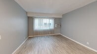 Located at 1830-1840 W Commonwealth Ave in Fullerton, CA, this single-story, one-bedroom, one-bathroom unit offers a practical and well-organized layout. Throughout the space, light wood-look flooring and soft gray walls create a clean, neutral aesthetic complemented by white trim and textured ceilings.

The combined kitchen and living area forms the heart of the unit. The living space features a large window dressed with vertical blinds, allowing natural light to fill the room, alongside a wall-mounted air conditioning unit for year-round comfort. The kitchen is equipped with white cabinetry and a sink, providing functional storage and workspace.

The bedroom is a well-proportioned private retreat, featuring a ceiling fan, a large window with vertical blinds for natural light, and a mirrored sliding closet that adds both storage and a sense of depth to the room.

The bathroom is finished in crisp white tile, featuring a full-size soaking tub with a handheld showerhead and chrome fixtures, along with a vanity sink and mirrored medicine cabinet.

A hallway connects the main living areas, contributing to an efficient and logical flow throughout the unit. The overall ambiance is bright, clean, and move-in ready, making it a straightforward and functional living space in a convenient Fullerton location.