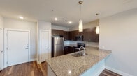 Located at 105 Newt Patterson Rd in Mansfield, TX, this single-floor residence offers a well-designed layout with contemporary finishes throughout. The open-concept kitchen serves as the heart of the home, showcasing rich dark cabinetry, granite countertops, a large center island with an undermount sink, and a full suite of stainless steel appliances including a refrigerator, range, and microwave. Elegant pendant lighting hangs above the island, adding a refined touch to the space. Wood-look plank flooring runs through the kitchen and living areas, providing a warm, cohesive aesthetic. The living area is bright and open, with track lighting and a ceiling fan adding both function and style. Bedrooms feature plush carpeting, ceiling fans, and windows with blinds that allow for natural light and privacy. The bathrooms are finished with granite vanity tops, dark wood cabinetry, and wood-look flooring. The primary bathroom includes a glass-enclosed shower and direct access to a walk-in closet, while the secondary bathroom offers a tub-shower combination with tile surround. Clean neutral wall tones and crisp white trim are consistent throughout, creating a modern and move-in-ready atmosphere.
