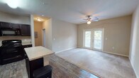 Located in Jacksonville, FL (32205), this single-floor unit offers a thoughtfully designed layout that balances functionality and comfort. The open-concept living area is a central highlight, featuring warm neutral tones, plush carpeting, and wood-look flooring that transitions seamlessly between spaces. A ceiling fan adds both style and practicality, while a set of French doors floods the room with natural light and provides access to an outdoor balcony with views of surrounding greenery.

The kitchen is well-appointed with rich, dark espresso cabinetry, granite-style countertops, a center island, and a full suite of black appliances including a refrigerator, range, microwave, and dishwasher. Wood-look flooring extends throughout the kitchen and entry area, adding a cohesive, polished look. Ample cabinetry ensures generous storage throughout.

The bedroom features soft carpeting, neutral wall tones, and a ceiling fan, creating a calm and restful environment. The bathroom is finished with tile surround in the tub/shower combination, wood-look flooring, a dark vanity with granite-style countertop, and brushed nickel fixtures. Additional features include an in-unit entry closet and utility access, contributing to the overall practicality of this well-maintained Jacksonville residence.