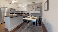 This single-floor residence offers a thoughtfully designed layout that balances comfort and functionality across its key living spaces. The kitchen is a standout feature, boasting crisp white shaker-style cabinetry, dark granite countertops, stainless steel appliances, and hardwood-style flooring that flows seamlessly into the adjacent dining area. The dining space is anchored by a textured accent wall with built-in wall-mounted shelving, creating a stylish backdrop for the dining setup. The living area provides a comfortable, open feel with ample room for relaxation.

The two bedrooms each carry their own distinct character. One features warm hardwood-style flooring, a soft grey accent wall, a double closet with louvered doors, wall-mounted corner shelving, and a window with natural light. The second bedroom offers a calming light blue accent wall, hardwood-style flooring, and a bright window, lending the room an airy, serene atmosphere.

Both bathrooms are finished with dark-toned vanity cabinetry paired with single-basin sinks, large mirrors, and tub-shower combinations with curtains. Light tile flooring adds a clean, polished look to each bathroom. Throughout the residence, consistent finishes and neutral tones create a cohesive and modern aesthetic.