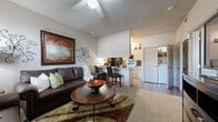 Located at 2112 S Santa Fe Ave in Moore, Oklahoma, this one-bedroom, one-bathroom unit is thoughtfully designed to maximize every square foot of its compact footprint. The open-concept layout seamlessly connects the living room and kitchen, creating a functional and inviting common area. The living room features vaulted ceilings with a ceiling fan, a textured ceiling finish, wood-look flooring, and large windows that allow natural light to fill the space. The kitchen is efficiently arranged in a galley style, equipped with light wood cabinetry, a stainless steel sink, a full appliance suite including a black refrigerator, electric range, and dishwasher. A granite-topped breakfast bar with bar seating bridges the kitchen and living area, ideal for casual dining. The bedroom offers plush carpeting, a generously sized window with exterior views, and ample wall space. The bathroom includes a tub and shower combination enclosed by sliding glass doors. Additional practical features include an in-unit washer and dryer area visible from the main living space. Throughout the unit, neutral wall tones and consistent flooring choices contribute to a cohesive and move-in-ready atmosphere.
