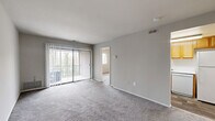 Located at 11 Cinnamon Cir in Randallstown, Maryland, this 2-bedroom, 1-bathroom residence offers a practical and efficient single-floor layout. The living area is carpeted in neutral-toned plush carpet and features a sliding glass door dressed with vertical blinds, allowing natural light to filter in while providing direct access to an outdoor balcony with exterior views. The open feel of the main living space is enhanced by clean white ceilings with overhead ventilation and a connected view into the second bedroom. The generously sized primary bedroom is carpeted and bathed in natural light from a wide window with exterior views, and includes a closet for storage. The second bedroom is also carpeted and features its own window, providing comfortable and functional space. The kitchen is equipped with warm honey-toned wood cabinetry, light countertops, a stainless steel sink, and white appliances including a range, dishwasher, and full-size refrigerator, all set atop wood-look flooring. The full bathroom features a tub-shower combination with white subway tile surround, a toilet, and a vanity sink, complemented by rich wood-look vinyl flooring that adds warmth to the otherwise crisp, neutral-toned space.