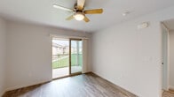 This single-story unit is designed with a clean, neutral aesthetic that emphasizes functionality and natural light. The open-concept living and dining area is anchored by light-toned hardwood-style flooring and a ceiling fan with an integrated light fixture. A sliding glass door leads directly to a private balcony with metal railing, offering views of surrounding green landscaping and neighboring buildings, allowing natural light to fill the space throughout the day.

The kitchen is efficiently laid out with gray cabinetry, white countertops, a peninsula with seating overhang, stainless steel appliances including a refrigerator, range, and over-the-range microwave, as well as a stainless steel sink positioned beneath a window. Recessed lighting enhances the kitchen's brightness.

The bedroom features plush wall-to-wall carpeting, a ceiling fan, and a window with horizontal blinds that provide natural light and views of the exterior. The bathroom is well-appointed with a wide gray vanity offering generous storage, a large wall-mounted mirror, light-toned hardwood-style flooring, and a window for ventilation. The overall ambiance throughout the unit is bright, clean, and move-in ready.