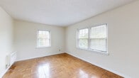 Located at 2907 North High Street in Columbus, Ohio, this one-bedroom, one-bathroom unit offers a practical and well-organized layout across a single floor. The spacious living room is a standout feature, showcasing warm parquet wood flooring in a classic block pattern that extends throughout the main living areas. Multiple windows allow natural light to fill the room, creating a bright and airy atmosphere, while a ceiling fan adds comfort. The neutral white walls provide a clean, versatile backdrop throughout the unit. The bedroom continues the parquet flooring theme and includes a closet, with natural light filtering in through a window. A hallway connects the main spaces efficiently. The kitchen features tile flooring, white cabinetry, a light countertop, a black refrigerator, and a stove, along with a window overlooking greenery outside. A wall heating unit is present in multiple rooms for climate control. The bathroom is fully tiled in warm earth tones, complete with a soaking tub, a pedestal sink, a mirrored medicine cabinet, and a window that provides natural ventilation. The overall ambiance of this unit is clean, functional, and classic — well-suited for comfortable everyday living.