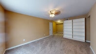 This single-floor space offers a practical and comfortable layout spread across several well-defined rooms. The living area serves as a welcoming entry point, featuring warm neutral-toned walls, plush carpeting, a ceiling fan with light fixture, and a window that allows natural light to filter in. Each bedroom continues the neutral color palette, with carpet flooring, ceiling fans, and windows dressed with blinds. One of the larger bedrooms features warm golden-yellow walls and a built-in white shelving unit, offering generous storage and display space alongside an additional walk-in or closet area. The kitchen is outfitted with white cabinetry, granite-style countertops, a tile backsplash in earthy tones, a double stainless steel sink, and a black dishwasher, all set above hardwood-style flooring. The bathrooms are clean and functional, each featuring a full tub and shower combination with white square tile surrounds, hardwood-style flooring, and standard fixtures. Ceiling fans are present throughout the living and sleeping areas, contributing to comfortable climate control. The overall ambiance is understated and move-in ready, with a consistent neutral color scheme that lends itself well to a variety of interior styles.
