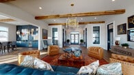 Located on Squires Circle in Lexington, Kentucky, this thoughtfully designed single-story clubhouse blends contemporary style with warm, transitional elements throughout its open layout. Rich hardwood flooring runs continuously across the space, complemented by exposed wood ceiling beams that add rustic character against crisp white walls and black-framed windows and doors.

The entrance foyer makes a strong first impression with double glass doors flanked by floor-to-ceiling windows, curated wall art, leather seating, and a bold brass chandelier overhead. Beyond the foyer, a generous lounge area serves as the heart of the space, furnished with tufted leather club chairs, a teal sofa, a wood coffee table, and a vibrant area rug. A gold multi-arm chandelier anchors the room, while abundant natural light streams through large windows.

Adjacent to the lounge is a dining and meeting area featuring a long bar-height table with upholstered seating, illuminated by a striking geometric gold pendant light. A built-in wet bar with deep blue cabinetry, gold hardware, and bold artwork creates a dramatic focal point in this area.

An interior overlook with sleek cable railings and floor-to-ceiling windows offers expansive outdoor views, bringing in natural light and a strong connection to the surrounding landscape.
