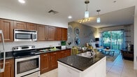 Located at 1517 Cameron Samuel Ln in West Palm Beach, FL, this well-appointed one-bedroom, one-bathroom residence offers a thoughtfully designed open-concept layout. Light-toned tile flooring flows throughout the main living area, connecting the kitchen, dining room, and living room into one cohesive, airy space.

The kitchen is a standout feature, equipped with rich wood cabinetry, dark granite countertops, a central island with a sink, stainless steel appliances including an electric range and built-in microwave, and a classic subway tile backsplash. Pendant lighting above the island adds a refined touch. The living area is bathed in natural light through sliding glass doors that open onto a private balcony, offering a seamless indoor-outdoor connection.

The bedroom is carpeted for comfort and is generously proportioned, accompanied by three closets, including a walk-in closet with wire shelving for ample storage. The bathroom mirrors the kitchen's design language with matching wood cabinetry, granite countertops, and a full tub-shower combination with tile surround.

Additional conveniences include an in-unit laundry area. The entry foyer, accented by recessed lighting and clean white walls, provides a welcoming arrival experience throughout this well-designed West Palm Beach residence.