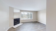 This efficiently designed 2-bedroom, 1-bathroom residence offers a well-organized single-floor layout with a cohesive, neutral aesthetic throughout. The living area serves as the heart of the home, featuring wood-look flooring, a classic fireplace with a white mantle, and a large window fitted with blinds that frames views of surrounding greenery, allowing natural light to fill the space. A baseboard heating system runs along the perimeter, ensuring year-round comfort. Adjacent to the living area, a built-in open shelving unit provides convenient storage, connecting seamlessly to the galley-style kitchen. The kitchen is outfitted with gray cabinetry, white countertops, a full-size refrigerator, and a dishwasher, maximizing functionality within a compact footprint. The primary bedroom features plush carpeting, a ceiling fan with light fixture, a mirrored sliding-door closet, and a window overlooking outdoor greenery. The secondary bedroom also offers carpeted flooring and a mirrored closet. The full bathroom includes wood-look tile flooring, a single-sink vanity with gray cabinetry, and a full tub-shower combination. A hallway connects all rooms, contributing to an efficient and practical flow throughout the residence.