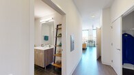 Located at 1965 N Milwaukee Ave in Chicago's vibrant Bucktown neighborhood, this modern single-floor unit offers a thoughtfully designed layout with clean, contemporary finishes throughout. The open-concept living area is anchored by expansive floor-to-ceiling windows that flood the space with natural light and provide sweeping views of the surrounding cityscape. Dark hardwood flooring runs through the main living areas, creating a warm contrast against the crisp white walls and high ceilings.

The kitchen is sleek and well-appointed, featuring a combination of white gloss upper cabinetry and light wood-toned lower cabinets, white quartz countertops, a classic subway tile backsplash, and a full suite of stainless steel appliances including a French door refrigerator, gas range, microwave, and dishwasher. A deep undermount sink completes the functional and stylish workspace.

The hallway connects the living areas to the bedroom and bathroom with ease. The bathroom features large-format tile flooring, a modern floating wood vanity with a wide mirror and bright vanity lighting, and a lean ladder shelf for additional storage. The bedroom is calm and understated, with neutral tones, clean walls, and a quiet ambiance well-suited for rest. A wall-mounted HVAC unit serves the living space, ensuring year-round comfort throughout this polished urban residence.