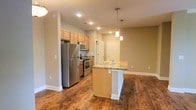 Located in the charming Olde Towne neighborhood, this single-floor space offers a thoughtfully designed open-concept layout that seamlessly blends the kitchen and living areas. The kitchen is a standout feature, equipped with stainless steel appliances including a refrigerator, gas range, and built-in microwave. Warm honey-toned wood cabinetry provides ample storage, while granite countertops lend a polished, modern feel. A central kitchen island with a built-in sink and pendant lighting above serves as both a functional workspace and a natural gathering point. Recessed lighting throughout keeps the space bright and welcoming. Rich, dark hardwood-style flooring runs continuously across the open floor plan, adding warmth and cohesion to the interior. Neutral, earthy wall tones complement the natural materials and create a calm, inviting ambiance. The open layout ensures excellent flow between the kitchen and the adjacent living area, making the space feel expansive and versatile. The entry door, visible from the kitchen, is conveniently accessible and well-integrated into the overall floor plan. This move-in-ready space combines contemporary finishes with a practical, comfortable design suited for everyday living.