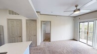 This one-bedroom, one-bathroom unit in Austin, TX offers a practical and well-appointed layout across a single floor. The living area features plush carpeting, crown molding, and a ceiling fan, with sliding glass doors that open to a balcony and invite natural light and outdoor views into the space. The kitchen is thoughtfully designed in a galley style, showcasing white shaker cabinetry, quartz countertops, a tile backsplash, stainless steel appliances including a refrigerator, microwave, and electric range, and durable wood-look flooring. A dedicated laundry area is conveniently accessible directly from the kitchen. The bedroom is a comfortable size, outfitted with soft carpeting, a ceiling fan, and a window with blinds that frames views of surrounding greenery. Crown molding adds a subtle architectural detail throughout. The bathroom features a full tub-shower combination with white tile surround, a quartz vanity top, and wood-look flooring. A closet provides additional storage. The unit's neutral color palette of warm beige and white tones creates a clean, cohesive ambiance throughout.