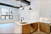 This contemporary 640 square foot apartment showcases a perfect blend of industrial and modern design elements. The single-floor layout comprises one bedroom, one bathroom, and an open-concept living area. High ceilings with exposed ductwork and black metal beams create a loft-like atmosphere, while large windows flood the space with natural light.

The kitchen is a standout feature, boasting a mix of white and wood cabinetry, stainless steel appliances, and a stylish backsplash. A central island with a sink and ample counter space serves as both a functional workspace and a casual dining area. Pendant lighting adds a touch of industrial chic.

The bedroom, measuring 160 square feet, includes a built-in closet system for maximized storage. The bathroom features a modern vanity, large mirror, and sleek fixtures. Throughout the apartment, light wood-look flooring complements the crisp white walls, creating a bright and airy ambiance.

Attention to detail is evident in the black-framed windows, recessed lighting, and carefully chosen hardware. This thoughtfully designed space efficiently utilizes every square foot, offering a perfect balance of style and functionality for modern urban living.