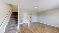 This two-story home offers a practical and well-organized layout spread across two evenly sized floors. The main level features a open living room finished with warm wood-look laminate flooring, neutral gray walls, and a textured ceiling with recessed lighting. A carpeted staircase leads to the upper level, while hallways connect the living area to the remaining rooms. The combined dining and kitchen area is a standout feature, showcasing white shaker-style cabinetry, granite countertops, a peninsula, subway tile backsplash, and stainless steel appliances including a refrigerator, electric range, and microwave. A window above the sink provides natural light. One bathroom on the main level features a granite-topped vanity and wood-look flooring. The upper level houses all three bedrooms, each finished with neutral carpet and windows that bring in natural light. The primary bedroom offers a modest, functional layout. Additional bathrooms on this floor include a tub/shower unit. A dedicated closet provides storage. Throughout, the home maintains a clean, neutral palette suited to a variety of furnishing styles.