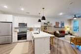 Located at 4720 Nations Crossing Rd in Charlotte, NC, this well-appointed one-bedroom, one-bathroom residence offers a thoughtfully designed open-concept floor plan. Light wood-style flooring flows throughout the main living areas, lending a cohesive and contemporary feel to the space.

The kitchen is a standout feature, showcasing crisp white cabinetry with gold-toned hardware, a soft green tile backsplash, and a full suite of stainless steel appliances including a range, over-the-range microwave, and refrigerator. A central white quartz island with an undermount sink provides both additional prep space and casual seating, with elegant pendant lighting above. The kitchen opens seamlessly into the living area, which benefits from a ceiling fan, a glass-paned door allowing natural light, and ample room for comfortable furnishings.

The bedroom offers a calm retreat with plush carpeting, a ceiling fan, a natural light-admitting window, and direct access to a dedicated closet. A secondary door connects to the hallway, enhancing the room's functional flow.

The bathroom is finished with subway tile surrounding a soaking tub and shower combination, wood-look flooring, and a clean white vanity with black fixtures. Clean-lined interior doors with matte black hardware complete the modern aesthetic throughout this well-crafted Charlotte residence.
