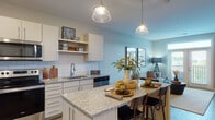This single-floor residence on Maple Street in Lawrenceburg, Indiana offers a thoughtfully designed layout with modern finishes throughout. The kitchen serves as a central highlight, featuring granite countertops, white shaker-style cabinetry, a classic subway tile backsplash, and a full suite of stainless steel appliances including a refrigerator, range, and built-in microwave. An island with bar seating and pendant lighting above creates an inviting space for casual dining and meal preparation. Light wood-tone flooring runs through the kitchen and living areas, contributing to a warm, cohesive aesthetic.

The living room is bright and welcoming, anchored by French doors that open to a private balcony, allowing ample natural light and outdoor views to enhance the interior. The space accommodates comfortable seating arrangements and offers a relaxed yet contemporary ambiance.

The bedroom features plush carpeting, large windows with natural light, a ceiling fan, and generous room for furnishings. The bathroom continues the refined design language with granite countertops, a wood-toned vanity, a framed mirror, and hardwood-style flooring.

Overall, the unit presents a clean, modern aesthetic with quality finishes, functional flow between spaces, and thoughtful details throughout.