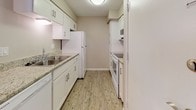 This single-floor residence offers a clean, modern aesthetic defined by neutral warm-beige walls, crisp white trim, and durable wood-look flooring that flows consistently throughout the space. The living area is generously sized, providing an open and airy feel with ample room for a variety of furniture arrangements. It connects seamlessly to the dining area, which is accented by a classic chandelier that adds a touch of elegance to the space.

The kitchen is designed in a galley layout, featuring white cabinetry with sleek hardware, granite-style countertops, white appliances including a refrigerator, oven, and built-in microwave, as well as a double sink. A pass-through breakfast bar separates the kitchen from the living and dining areas, enhancing the open flow of the floor plan.

The bedrooms are well-proportioned, each featuring wood-look flooring and neutral walls that create a calm and restful atmosphere. Closet storage is provided, with louvered and sliding closet doors visible in the rooms, offering practical organization solutions.

The bathroom is efficiently arranged with a shower/tub combination, a toilet, and wood-look flooring that ties the space together with the rest of the home. Natural light filters into several rooms, contributing to the overall bright and welcoming ambiance of this thoughtfully laid-out residence.