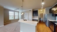 Located at 2013 Copper Leaf Pkwy in Durham, NC, this single-floor residence offers a thoughtfully designed layout with a warm, neutral color palette and crown molding throughout. The open-concept kitchen serves as a central hub, showcasing dark espresso cabinetry, a light-toned subway tile backsplash, stainless steel appliances including a range, microwave, and refrigerator, and a generous peninsula island with a built-in sink and pendant lighting above. Hardwood flooring runs through the kitchen and entry areas, while plush carpeting extends into the living and bedroom spaces. The expansive living area benefits from multiple windows fitted with blinds, allowing ample natural light, and is complemented by track lighting and a ceiling fan. Bedrooms are spacious and well-lit, with one featuring built-in shelving and a desk surface, offering functional storage solutions. The bathrooms are finished with beige tile surrounds, soaking tubs with shower combinations, and wood-look flooring. Additional features include louvered closet doors, arched interior doorways, and a well-organized walk-in closet. The overall ambiance is clean, functional, and move-in ready.