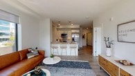 This two-bedroom, two-bathroom residence at 1011 Washington Blvd in Stamford, Connecticut offers a thoughtfully designed single-floor layout with a clean, contemporary aesthetic throughout. The open-concept living and kitchen area serves as the heart of the home, where light wood-style flooring, bright white walls, and large floor-to-ceiling windows combine to create an airy, sun-filled atmosphere with sweeping city views. The kitchen is outfitted with white cabinetry, stone-topped counters, a full suite of stainless steel appliances, and a breakfast bar with seating — ideal for casual dining or entertaining. A dedicated dining nook with pendant lighting provides a more formal eating space. The living room benefits from expansive windows that frame city and treetop views, filling the space with natural light. Both bedrooms are generously proportioned with wood-style flooring and large windows; the primary bedroom features city views and ample room for a full furniture arrangement. The two bathrooms are finished in a modern style — one featuring a glass-enclosed walk-in shower with tile surround, and the other a clean, white vanity with tile flooring. A dedicated in-unit laundry closet with a stacked washer and dryer adds everyday convenience to this well-appointed Stamford residence.