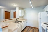 Located at 9121 Waterside St in Madison, WI, this well-appointed one-bedroom, one-bathroom residence offers a practical and comfortable single-floor layout. The open-concept kitchen and living area serves as the heart of the home, with the kitchen featuring white cabinetry, white appliances including a refrigerator, electric range, and microwave, a double-basin sink, and light countertops. Track lighting illuminates the kitchen workspace, while durable wood-style flooring extends throughout this zone. A curved peninsula counter separates the kitchen from the entry area, adding both style and function. In-unit stacked laundry is conveniently tucked nearby. The living room is carpeted and bathed in natural light, with a sliding glass door opening to a private balcony that overlooks greenery — a welcoming outdoor retreat. The spacious bedroom features plush carpet, a ceiling fan with light, and a large window framing views of mature trees, providing a bright and serene atmosphere. The full bathroom includes a white vanity with a single sink, a tub-shower combination, and a well-lit vanity mirror. A dedicated closet provides additional storage. Wood-tone trim and clean, neutral walls tie the space together throughout.