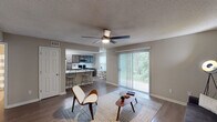 This single-story, two-bedroom, two-bathroom residence in Pensacola, Florida offers a well-designed open floor plan with modern finishes throughout. The living area serves as the central hub of the home, featuring wood-style flooring, a ceiling fan, and a large sliding glass door fitted with vertical blinds that floods the space with natural light and provides views of the surrounding greenery. The open-concept layout connects the living area directly to the kitchen, which is well-appointed with dark cabinetry, marble-style countertops, a white subway tile backsplash, and a full suite of stainless steel appliances including a refrigerator, over-the-range microwave, and electric range. A dedicated dining nook adjacent to the kitchen benefits from a window overlooking the outdoors. An in-unit laundry area is conveniently accessible from the kitchen. Both bedrooms are carpeted and include ceiling fans and closet storage. The primary bedroom features an en-suite bathroom with a dark-cabineted vanity and marble-style countertop. The second full bathroom mirrors this aesthetic. Textured ceilings are consistent throughout the home.