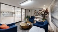 Located at 57 Widdicombe Hill Blvd in Toronto, this shared laundry facility offers a well-organized and functional space designed to serve building residents with ease and comfort. The main laundry area is finished with clean white floor tiles and features a horizontal band of beige and light blue wall tiles that run along the perimeter, giving the room a tidy, institutional character. Bright fluorescent lighting illuminates the space throughout.

The laundry room is equipped with a row of front-loading washing machines and a bank of stacked dryers, providing substantial capacity. A built-in counter with white cabinetry and an integrated utility sink runs along one wall, offering a practical folding and sorting surface. A large mirror above the counter enhances the sense of openness. A bulletin board near the entrance displays notices and information for residents.

Adjacent to the laundry area, separated by glass sliding doors, is a comfortable resident lounge that elevates the overall experience of the facility. This sitting area features plush blue armchairs arranged around a round gold coffee table and white marble side tables, set atop patterned carpet. A built-in bookshelf stocked with a wide selection of reading materials, indoor plants, and a large abstract wall painting contribute to a welcoming and relaxed atmosphere, making the wait time an opportunity to unwind.