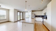 Located at 5430 Cane Ridge Rd in Nashville, TN, this well-appointed 2-bedroom, 2-bathroom residence offers a thoughtfully designed single-floor layout with modern finishes throughout. The open-concept living, dining, and kitchen area serves as the heart of the home, featuring light hardwood-style flooring, large windows that flood the space with natural light, and a sliding glass door leading to a private balcony with outdoor views. A ceiling fan adds comfort to the airy living area. The kitchen is outfitted with crisp white cabinetry, a dark slate tile backsplash, stainless steel appliances including a refrigerator, range, and microwave, and a spacious central island with a built-in sink and pendant lighting above. The entrance includes a built-in mudroom-style nook with shelving and hooks for added functionality. Hallways are bright and clean, enhanced by recessed lighting and tray ceiling details. The primary bedroom is generously sized with plush carpeting and features two walk-in closets with built-in shelving. The second bedroom also offers carpeted flooring and a walk-in closet. Both bathrooms are finished with marble-style tile flooring and white vanities. A dedicated laundry area and five closets round out the practical storage options throughout this well-designed Nashville home.