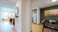 This thoughtfully designed one-bedroom, one-bathroom residence offers a cohesive single-floor layout that maximizes both functionality and comfort. Light-toned bamboo hardwood flooring flows seamlessly through the main living areas, lending warmth and continuity to the space.

The kitchen is a standout feature, showcasing rich warm-toned wood cabinetry, dark granite countertops, a full suite of stainless steel appliances — including a refrigerator, range, microwave, and dishwasher — and pendant lighting that adds a refined touch. The kitchen opens directly into the dining area, which is defined by a charcoal accent wall and connects naturally to the living room.

The living room is bright and welcoming, benefiting from large windows that invite generous natural light and offer pleasant outdoor views. The adjacent dining space provides an intimate setting suited for everyday meals or entertaining.

The bedroom is a comfortable retreat with plush carpeting, direct access to the bathroom, and a calm, understated aesthetic. The bathroom features dark slate-toned tile flooring, warm wood vanity cabinetry, and a clean, functional layout. A circular wall mirror near the entryway adds a stylish finishing detail to the overall design of the home.
