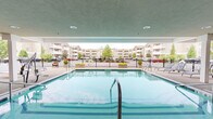 Located at 9500 Transit Rd in East Amherst, NY, this amenity space centers around a generously sized swimming pool positioned beneath a covered structure, offering year-round usability regardless of weather conditions. The pool is equipped with accessibility features, including a mechanical pool lift and sturdy handrail entry, ensuring inclusive access for all users. Recessed ceiling lighting illuminates the covered deck area, which is finished with a textured aggregate surface providing both durability and slip resistance.

Surrounding the pool, multiple lounge chairs are arranged along the deck, offering comfortable spaces for relaxation. A covered patio area runs adjacent to the pool and is accessible through a series of large French doors and expansive grid-pane windows, which allow natural light to flow freely between interior and exterior spaces. The patio is furnished with wicker seating, including a bench with colorful cushions and a dining set with chairs, creating a welcoming social environment.

The space is enclosed by a black iron fence that frames the pool perimeter, adding a layer of safety while maintaining open sightlines to the surrounding landscaped grounds and multi-story residential buildings beyond. Wall-mounted lantern-style light fixtures accent the exterior façade, contributing to the overall welcoming ambiance of this well-appointed communal amenity area.