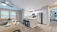 This well-appointed single-floor residence offers four bedrooms, two bathrooms, and a thoughtfully designed open-concept layout. The combined kitchen and living area serves as the heart of the home, bathed in natural light from multiple windows dressed with classic blinds. The kitchen features white shaker cabinetry, quartz countertops, stainless steel appliances — including a refrigerator, range, and microwave — and a peninsula with bar seating, ideal for casual dining. The living area accommodates both a comfortable lounge space and a dedicated dining area, complete with a ceiling fan overhead and light wood-look flooring throughout. The primary bedroom is generously sized, offering plush carpeting, a ceiling fan, and ample natural light, complemented by a spacious walk-in closet with wire shelving. Additional bedrooms are well-proportioned with soft carpeting and natural light. Both bathrooms are finished with white shaker vanity cabinetry, dual sinks where applicable, quartz countertops, and clean tile flooring. Neutral gray tones carry throughout the space, creating a calm and cohesive ambiance that is both modern and inviting.
