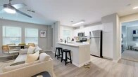 This well-appointed single-floor residence offers four bedrooms, two bathrooms, and a thoughtfully designed open-concept layout. The combined kitchen and living area serves as the heart of the home, bathed in natural light from multiple windows dressed with classic blinds. The kitchen features white shaker cabinetry, quartz countertops, stainless steel appliances — including a refrigerator, range, and microwave — and a peninsula with bar seating, ideal for casual dining. The living area accommodates both a comfortable lounge space and a dedicated dining area, complete with a ceiling fan overhead and light wood-look flooring throughout. The primary bedroom is generously sized, offering plush carpeting, a ceiling fan, and ample natural light, complemented by a spacious walk-in closet with wire shelving. Additional bedrooms are well-proportioned with soft carpeting and natural light. Both bathrooms are finished with white shaker vanity cabinetry, dual sinks where applicable, quartz countertops, and clean tile flooring. Neutral gray tones carry throughout the space, creating a calm and cohesive ambiance that is both modern and inviting.