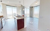 This single-floor urban residence showcases a compelling blend of industrial and contemporary design elements. Exposed concrete ceilings and structural columns contrast with clean white walls and warm wood-look flooring that flows throughout the space, creating a sophisticated industrial-modern aesthetic.

The entry corridor leads into an open-concept layout where the kitchen and living area integrate seamlessly. The well-appointed kitchen features rich dark-wood cabinetry, granite countertops, a subway tile backsplash, and a full suite of stainless steel appliances, including a gas range, built-in microwave, dishwasher, and French door refrigerator. A peninsula with pendant lighting provides additional prep space and connects the kitchen to the living area.

The living room is a bright, airy space anchored by floor-to-ceiling windows that flood the room with natural light and offer urban views. A sliding glass door opens to a private balcony furnished with outdoor seating. The exposed concrete ceiling adds an architectural focal point throughout.

The bedroom continues the floor-to-ceiling window motif, offering abundant natural light and direct balcony access through a glass door. A wall-mounted television adds convenience. The bathroom features tile flooring, a granite-topped vanity with dark wood cabinetry, and a separate shower enclosure. An in-unit washer and dryer provide added practicality.