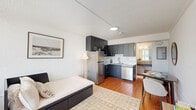 Located at 4455 W New Haven Ave in Melbourne, Florida, this thoughtfully designed studio unit makes efficient use of its compact single-floor footprint. The open-plan living area features warm wood-look tile flooring and crisp white walls, creating a bright and welcoming atmosphere. A large window near the entry door allows natural light to fill the space, while a textured ceiling adds visual depth throughout.

The kitchen is a standout feature, outfitted with dark charcoal cabinetry that extends floor to ceiling, offering generous storage. Stainless steel appliances — including a full-size refrigerator, built-in microwave, dishwasher, and a cooktop — are complemented by granite countertops and a classic white subway tile backsplash. The living and dining areas flow seamlessly from the kitchen, providing a functional and cohesive layout.

The unit includes two bathrooms, one of which features a granite-topped vanity with an open base, white tile walls, and a large mirror that reflects natural light from the adjacent window. A closet area with shelving provides practical storage.

The entryway offers additional living space with room for a small dining table and a console, completing this well-appointed, efficiently designed studio in Melbourne, FL.