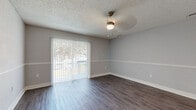 This single-floor residence offers a clean, modern aesthetic throughout, with consistent neutral gray walls, white trim, and a mix of wood-look and carpeted flooring that ties each space together cohesively. The living area is bright and welcoming, featuring dark hardwood-style flooring, a ceiling fan with light fixture, and a sliding glass door fitted with vertical blinds that opens to an outdoor balcony, allowing natural light to pour in and providing views of the surrounding greenery. A decorative chair rail runs along the walls, adding a touch of architectural detail. The kitchen is efficiently designed with white cabinetry, light speckled countertops, a stainless steel refrigerator, a white electric range, a dishwasher, and an under-cabinet range hood. A peninsula with a pendant light above creates a natural transition into the dining or living area, and a window above the sink brings in additional daylight. Sliding closet doors in the adjoining space offer practical storage. The bedroom features plush carpet flooring, a ceiling fan, and a large window with views of palm tree-lined surroundings. Two full bathrooms are finished in crisp white, each equipped with a tub-shower combination, toilet, white vanity cabinetry with brushed nickel hardware, and wood-look tile flooring. The overall ambiance is clean, neutral, and move-in ready.