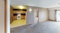 This single-floor, 3-bedroom, 2-bathroom residence offers a practical and comfortable layout designed for everyday living. The kitchen is well-equipped with ample maple cabinetry, deep countertops, and a full suite of white appliances including a range, microwave, dishwasher, and refrigerator. Light tile flooring and dark accent walls give the kitchen a bold, contrasting aesthetic. The open connection between the kitchen and the carpeted living area creates a seamless flow, with a wall sconce adding a warm ambiance to the shared space. Each of the three bedrooms features plush, neutral-toned carpeting and warm wood trim accents. Two of the bedrooms are brightened by pairs of windows with views to the outdoors, while the third offers a generous closet with a sliding wood-panel door. The two bathrooms are clean and functional: one includes a full tub-shower combination with a mirrored medicine cabinet and a wood-trimmed vanity, while the second features a standing shower, matching vanity, and mirrored storage. Textured ceilings and consistent trim details throughout the home provide a cohesive and well-maintained finish.