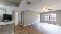 This single-floor unit is designed with a practical, open-concept layout that connects the living area and kitchen seamlessly. The living space is bright and airy, benefiting from natural light streaming through large windows and a glass sliding door that opens to an outdoor view of a grassy area. Warm-toned luxury vinyl plank flooring runs consistently throughout, providing a cohesive and low-maintenance finish. Ceiling fans are present in the main living area and bedrooms, ensuring comfortable airflow throughout.

The kitchen is efficiently laid out with white shaker-style cabinetry, a marble-look countertop with a peninsula overhang, and black appliances including a refrigerator, electric range, built-in microwave, and a stainless-steel sink. The neutral gray wall tones complement the white trim and cabinetry throughout the unit.

The bedrooms are comfortably sized, each featuring a ceiling fan, natural light from windows, and dedicated closet space. One bedroom includes a spacious walk-in closet outfitted with wire shelving, while another features a reach-in closet and sliding glass door access to the outdoors. The full bathroom is clean and functional, offering a tiled tub-shower combination, a vanity with a marble-look countertop, and a large mirror with overhead lighting.