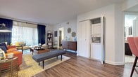 This single-floor residence showcases a cohesive mid-century modern aesthetic throughout its well-appointed rooms. The living area serves as the heart of the home, featuring wood-look flooring, a bold orange tufted sofa, a geometric-patterned area rug, and track lighting overhead — all complemented by abstract wall art and dark navy curtains that add depth and contrast to the bright white walls.

The kitchen is equipped with dark espresso cabinetry, granite countertops, stainless steel appliances including a range and refrigerator, and light tile flooring. A skylight adds natural brightness to the cooking space, which flows into a cozy dining nook.

The primary bedroom offers plush carpeting, a large window for natural light, and access to an en-suite bathroom featuring a vanity with granite countertops, dark cabinetry, a tub-shower combination, and a walk-in closet with built-in shelving. A secondary bedroom provides a comfortable retreat with carpet flooring, a wide window, and a reading nook with a sliding glass door offering an outdoor view. An additional bedroom is carpeted and bright, ideal as a guest room or flex space. Each room reflects a warm, intentional design sensibility throughout.