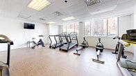 This state-of-the-art fitness center, located at 3545-3555 Ch de la Côte-des-Neiges in Montréal, spans 84 square meters on a single floor. The space is thoughtfully divided into distinct workout zones, each catering to different exercise needs. The cardio area features multiple treadmills and stationary bikes, while the strength training section is equipped with various weight machines and free weights. Large windows line the walls, flooding the space with natural light and offering views of the surrounding area. The facility boasts a clean, modern aesthetic with white walls, dropped ceilings with recessed lighting, and a combination of durable flooring materials including wood-look laminate and rubberized surfaces. Mirrors are strategically placed to enhance the sense of space and aid in proper exercise form. Additional amenities include wall-mounted TVs, exercise balls, and other functional training equipment, ensuring a comprehensive fitness experience for users of all levels.