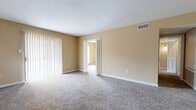 Located at 607 Hampton Cir in Jackson, MS, this single-story home offers four bedrooms and two full bathrooms across a well-organized floor plan. Warm beige walls and neutral carpet flooring are consistent throughout, creating a cohesive and understated aesthetic.

The spacious living room features a textured ceiling, vertical blind-covered sliding glass door, and an open passage connecting to adjoining rooms. The dining area is distinguished by decorative wainscoting panels, a pendant light fixture, and its own sliding glass door providing outdoor views and natural light.

The galley-style kitchen is equipped with dark wood cabinetry, light countertops, a white electric range, refrigerator, dishwasher, and tile flooring. A window above the sink adds natural light to the functional workspace.

The bedrooms are carpeted and bathed in natural light; the primary bedroom includes a ceiling fan and a large window with an outdoor view. Additional bedrooms are generously sized with neutral walls and ample space. A carpeted hallway connects the private areas of the home. The bathrooms feature wood vanities with light stone-style countertops and large mirrors. White trim and six-panel doors are present throughout, lending a clean, uniform finish to the interior.